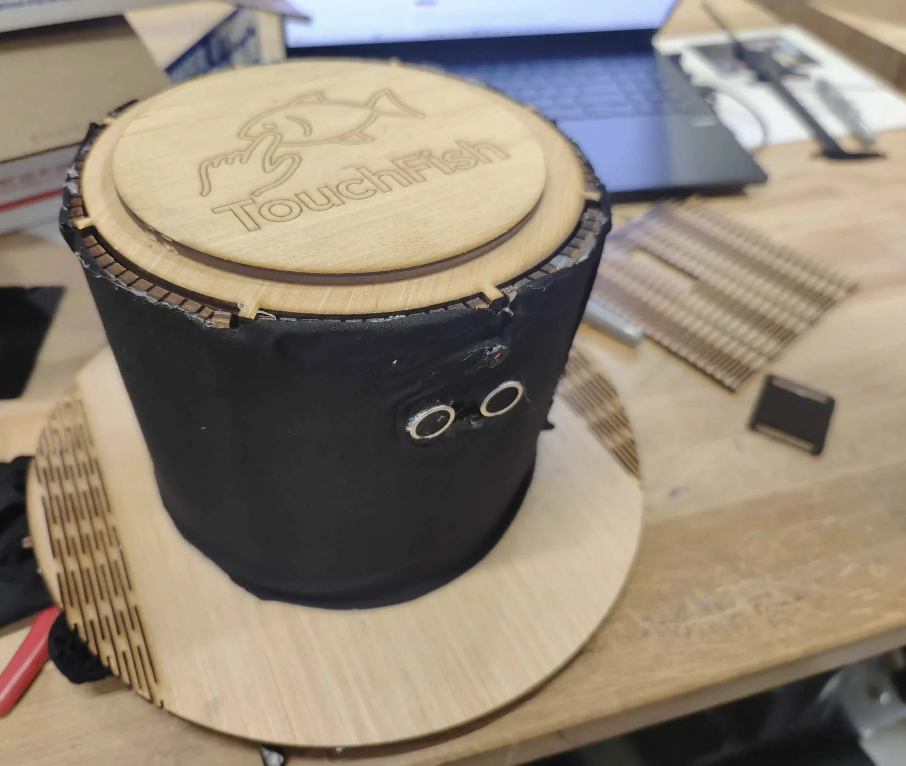 Black fabric-covered top hat with a plywood brim, two round sensors on the front and an engraved TouchFish lid.