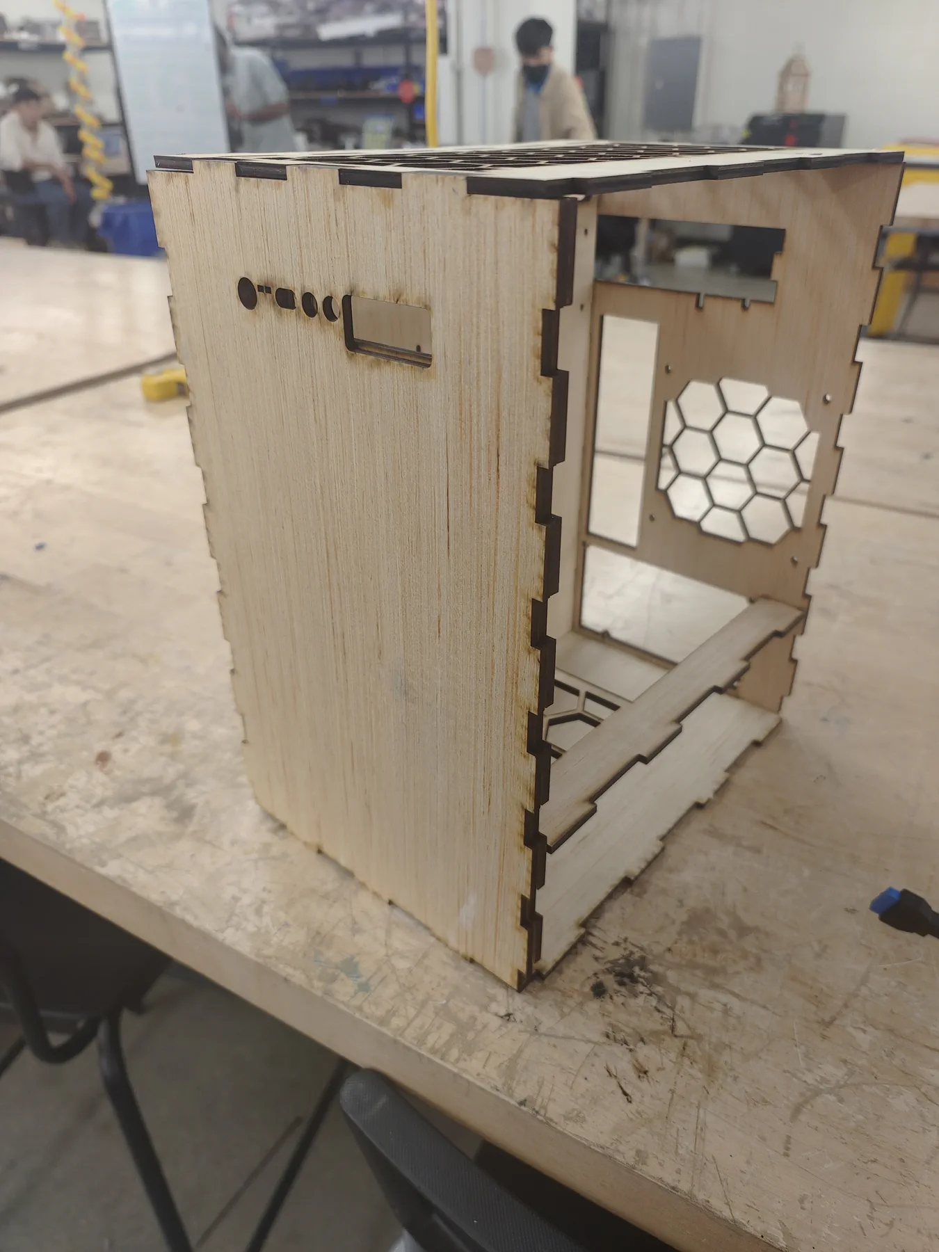 Empty laser-cut plywood PC case on a workshop table.