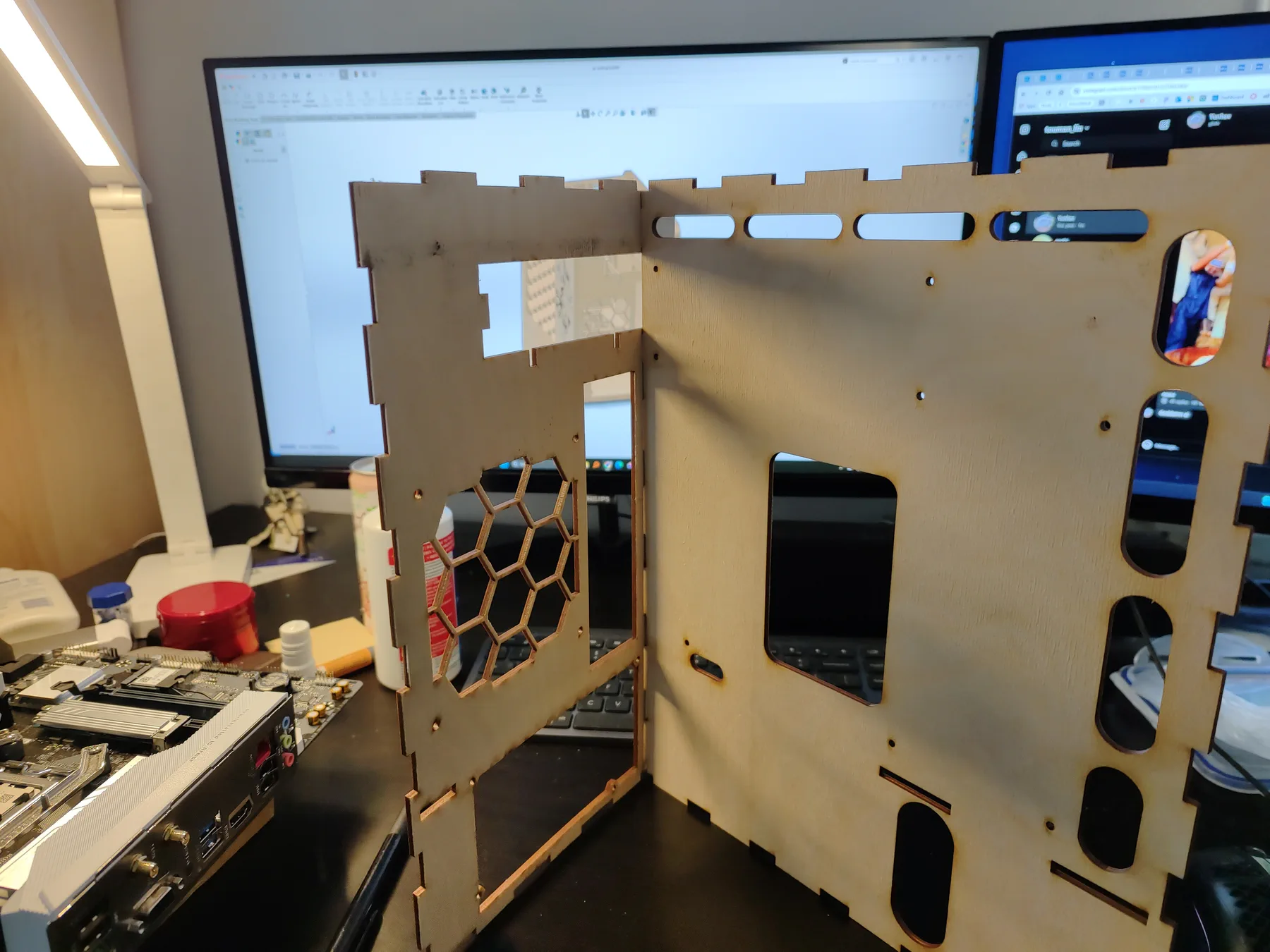 Two laser-cut plywood case panels standing on a desk in front of a monitor.