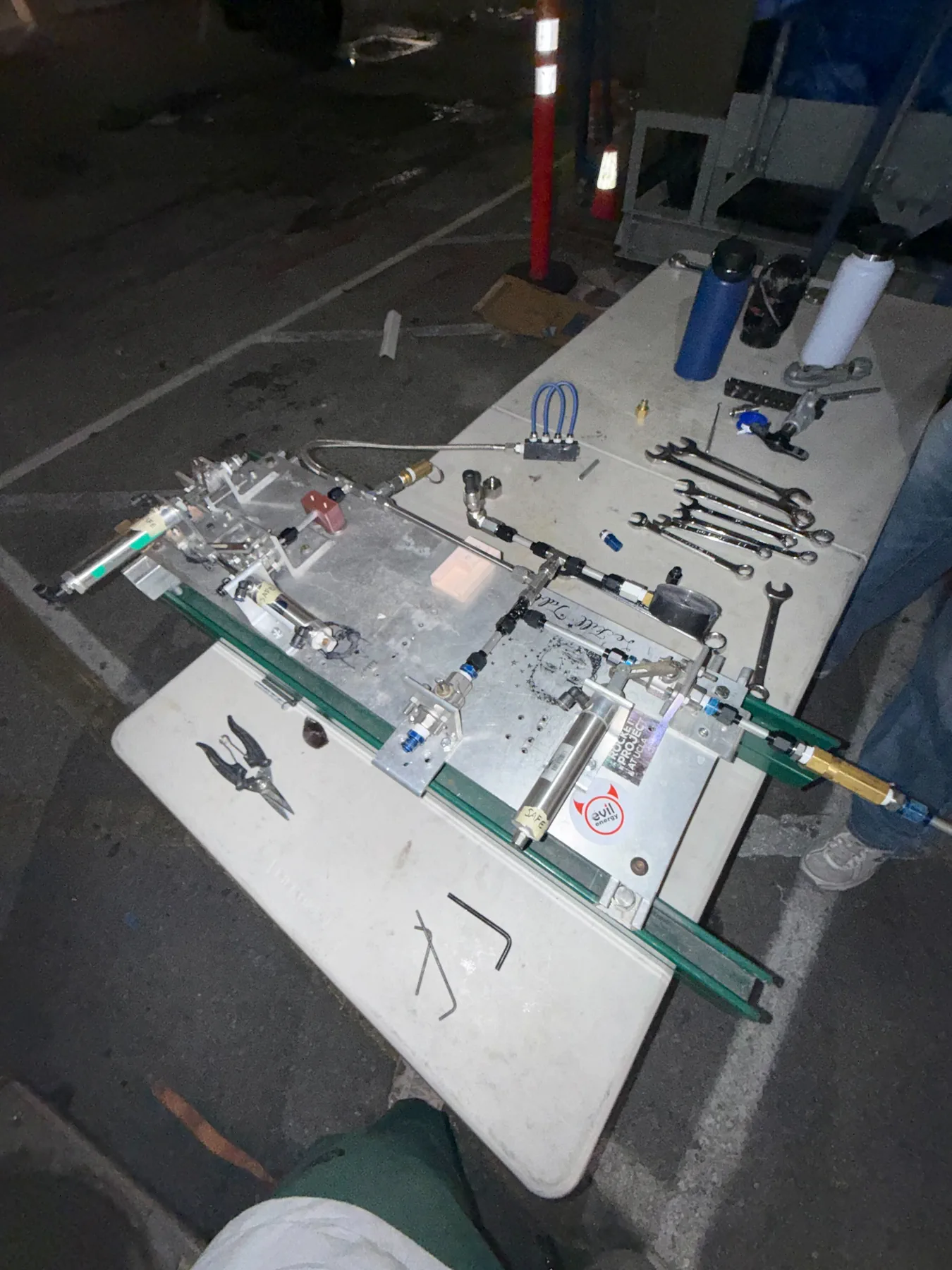 Rocket fill-table hardware on a white folding table at night, wrenches lined up next to it.