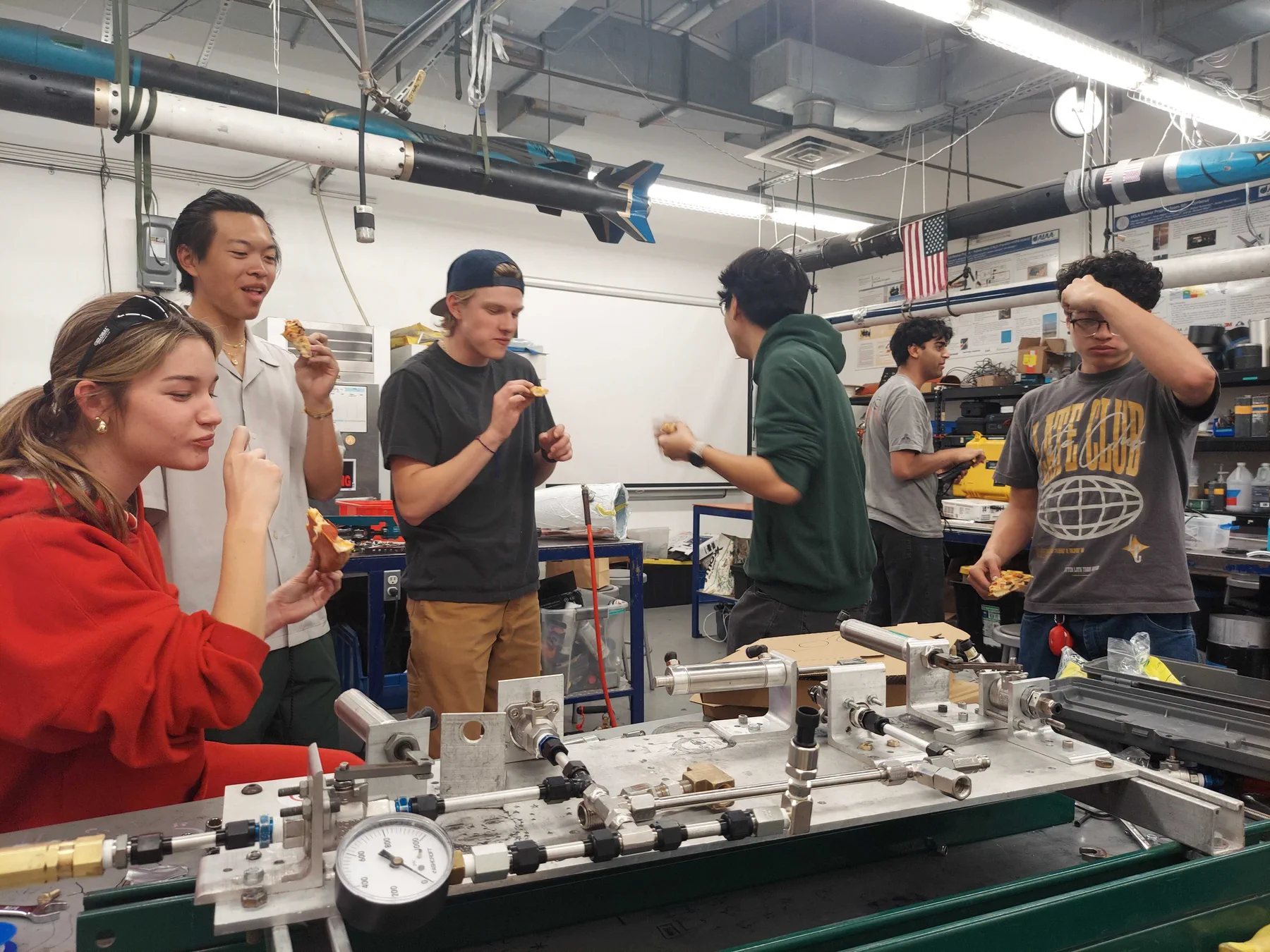 Students in a rocket lab standing behind a fill table of stainless tubing, valves and a pressure gauge.