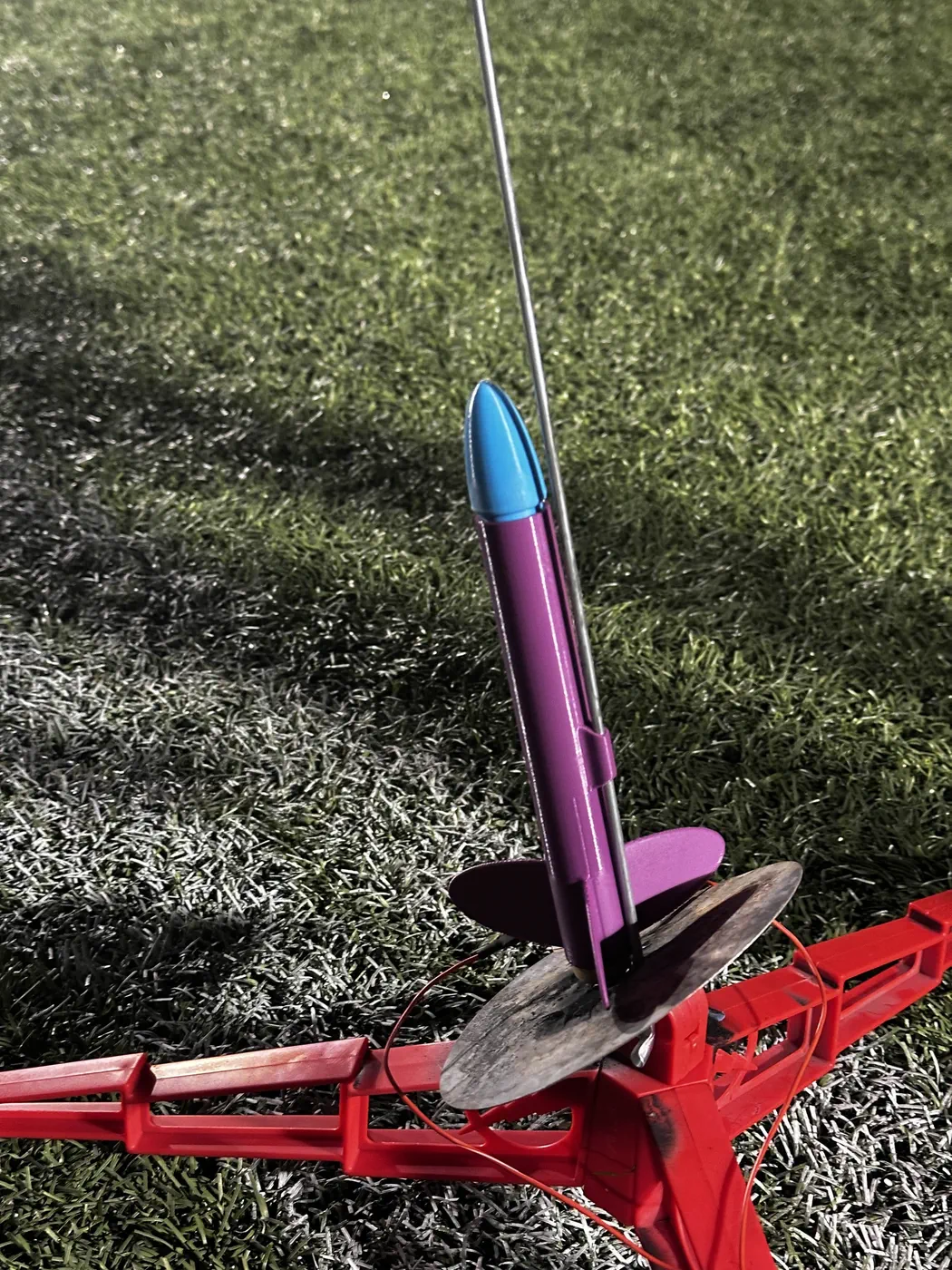 Purple model rocket with a blue nose cone on a red launch pad.