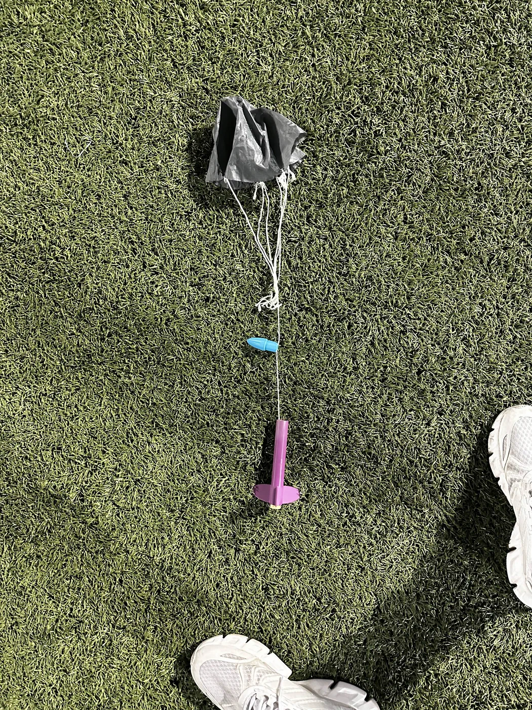Purple model rocket, blue nose cone and black parachute lying on artificial turf.