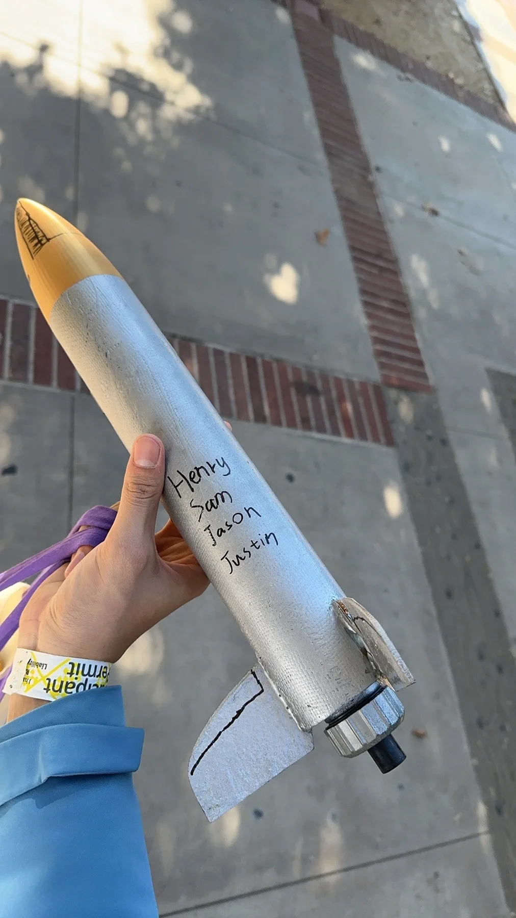 Hand holding a silver rocket with a gold nose cone and four names written on the body.